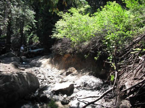 1991 Ford Bronco - A person stands near an off-road vehicle navigating a difficult, rocky path through a forest.
