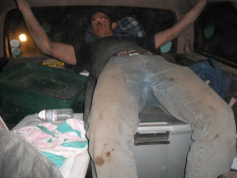 1991 Ford Bronco - A man rests in the cargo area of a vehicle, surrounded by various containers and blankets.