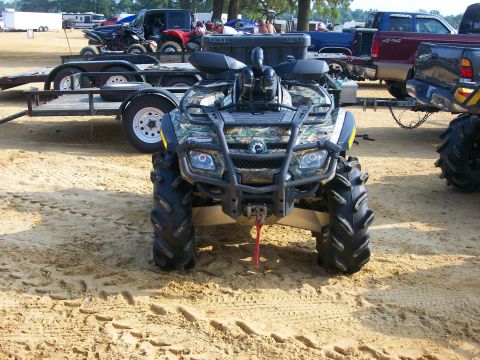 2008 Bombardier Outlander - A camouflage ATV sits on sandy ground with other vehicles visible in the background.