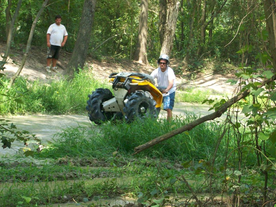 Yellow and white ATV on its side in a muddy creek as a rider pulls it upright