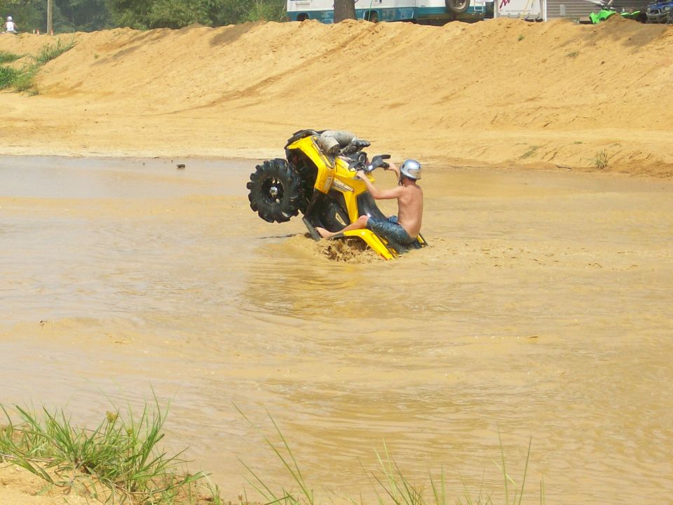 Rider wheelies a yellow ATV through a muddy water pit at an off-road park
