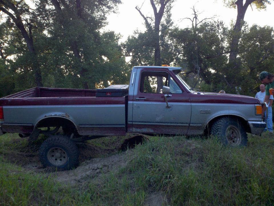 Maroon and silver pickup truck stuck in mud, side view. Appears to be a 1987 Ford F-150