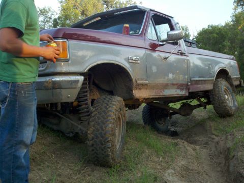 1988 Ford F-150 - A person stands next to a lifted Ford F-150 truck that is partially stuck in mud.