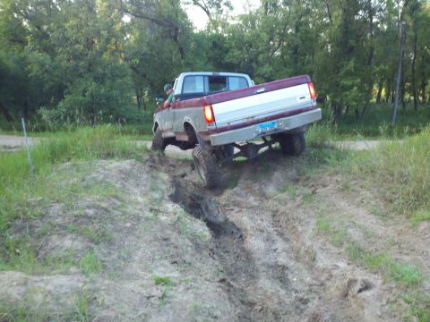 1988 Ford F-150 - A red and silver pickup truck navigates a muddy off-road trail.
