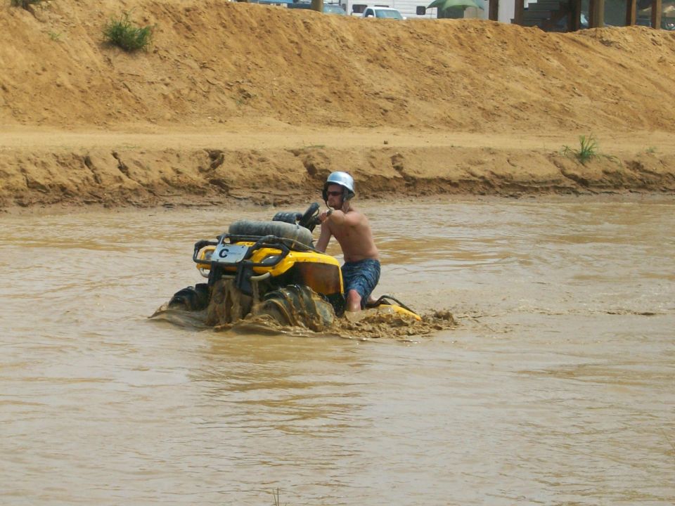 Yellow Can-Am ATV riding through a deep muddy water pit with rider standing off the seat