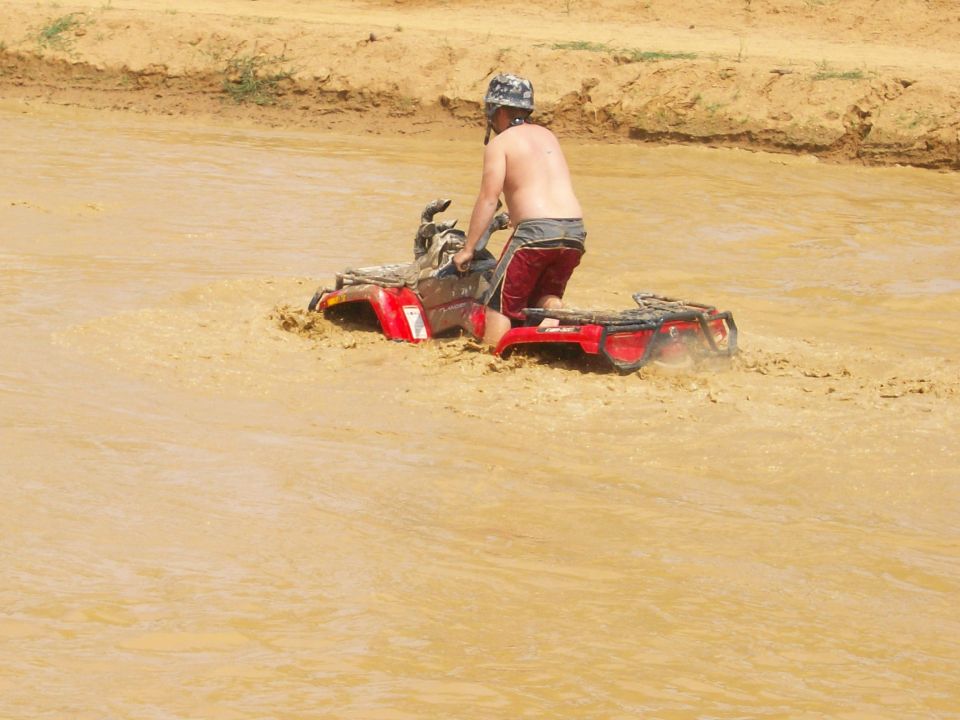 Rider standing on a red ATV crossing deep muddy water