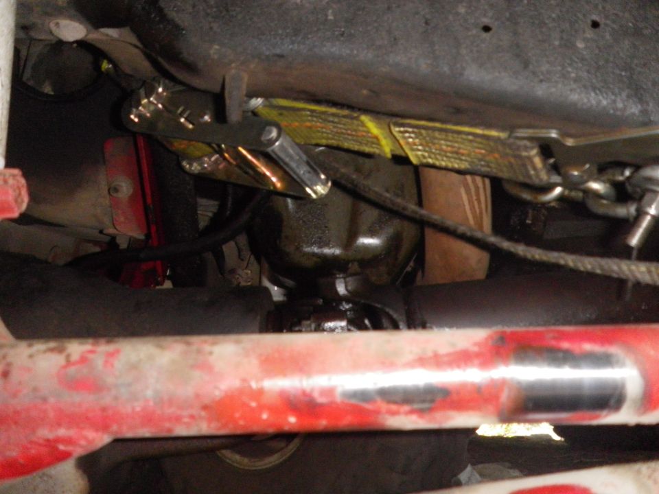 Close-up of vehicle undercarriage showing a strap and clamp mechanism attached to a component
