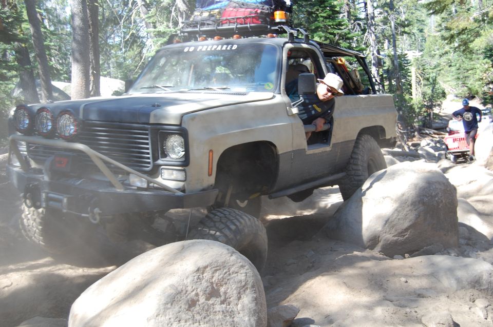 Modified pickup truck with off-road tires and lights navigating a rocky trail. Text on windshield reads 'GO PREPARED'