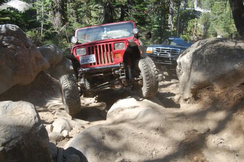 1993 Jeep Wrangler - A red 1993 Jeep Wrangler tackles a challenging off-road path with another vehicle following closely.