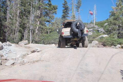 1993 Jeep Wrangler - This 1993 Jeep Wrangler is navigating a challenging off-road trail with trees and rocks surrounding it.