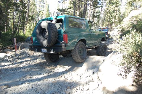 1993 Jeep Wrangler - Green SUV navigates a challenging rocky trail in a wooded area.