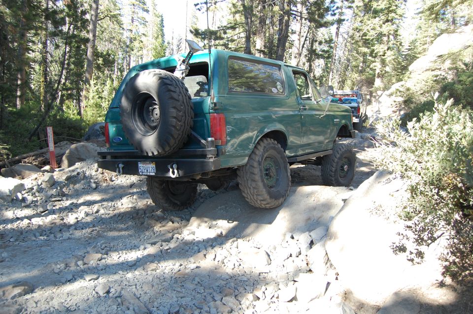Green SUV with spare tire on rear, driving on rocky terrain