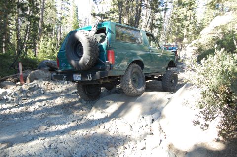 1993 Jeep Wrangler - Green 1993 Ford Bronco navigates a challenging rocky trail with a spare tire mounted on the rear.