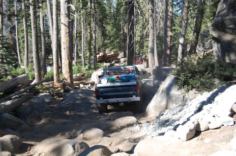 1993 Jeep Wrangler - Off-road adventure in a rocky forest environment with a pickup truck on a challenging trail.
