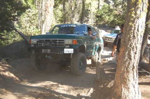 1993 Jeep Wrangler - Two off-road vehicles navigate a wooded trail, with the lead vehicle displaying a custom windshield decal.