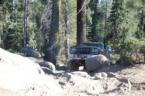 1993 Jeep Wrangler - This truck is off-roading on a dirt path surrounded by trees and large rocks.