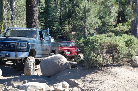 1993 Jeep Wrangler - A red Jeep Wrangler navigates a rocky off-road trail behind a blue pickup truck.