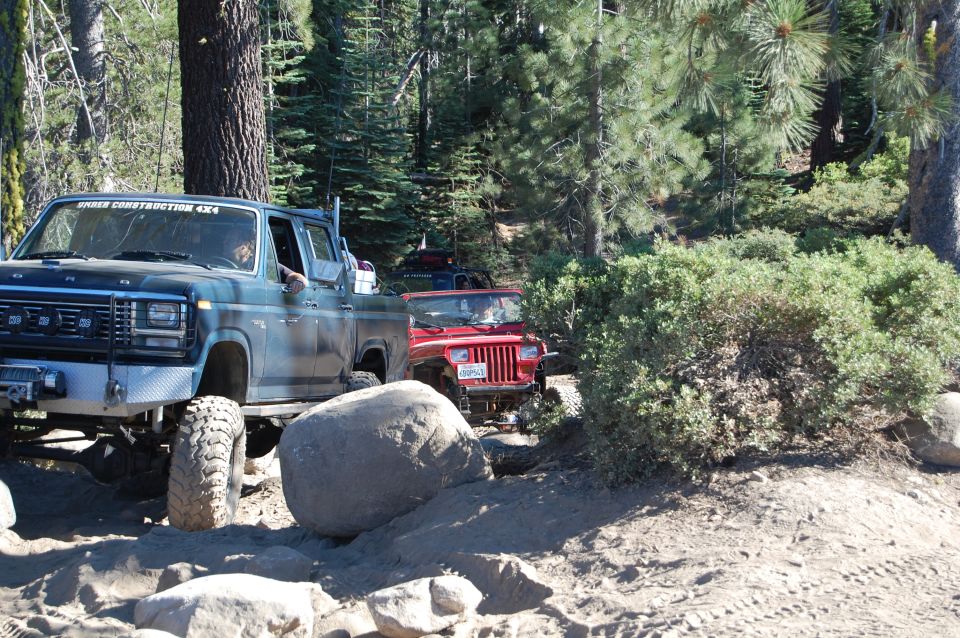 Red Jeep Wrangler on a dirt trail with a blue pickup truck