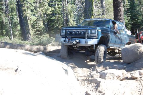 1993 Jeep Wrangler - This blue pickup truck is navigating a rocky off-road trail, with another vehicle visible in the background.