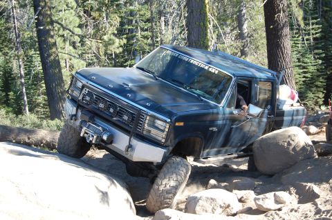 1993 Jeep Wrangler - This Ford F-Series truck is shown off-roading on a challenging, rocky terrain with trees in the background.
