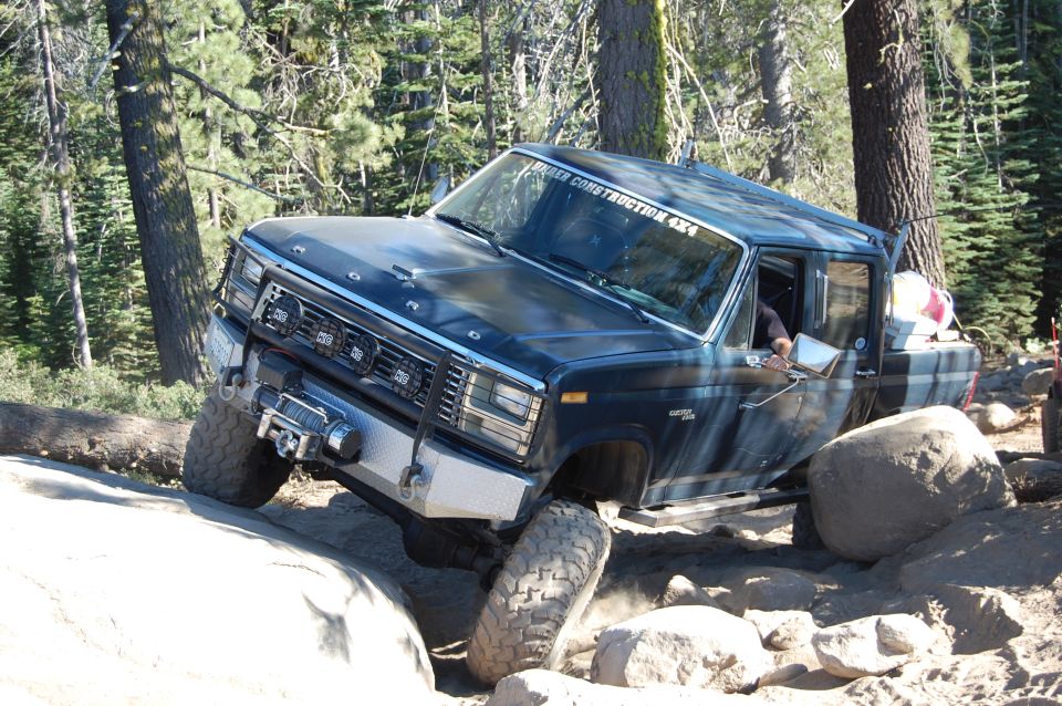 Dark blue Ford F-Series truck navigating a rocky trail, tires angled on boulders