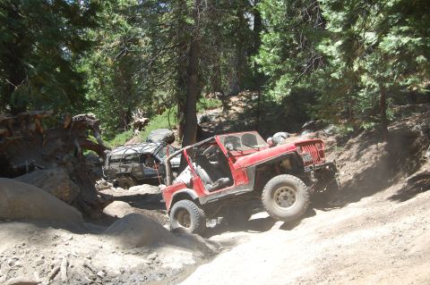 1993 Jeep Wrangler - Two off-road vehicles tackle a challenging rocky path through a forest.