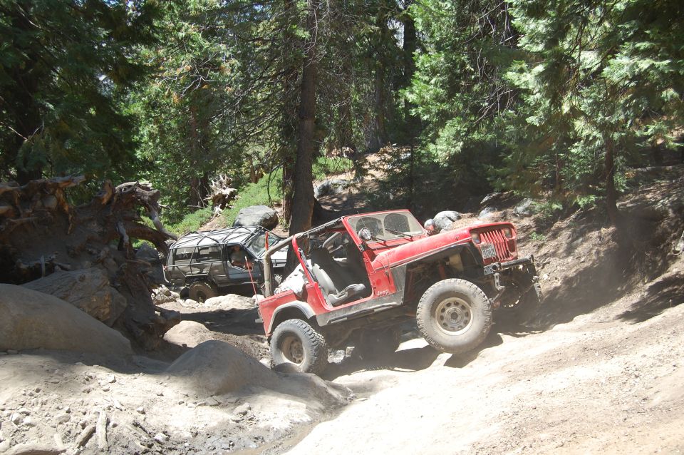 1993 Jeep Wrangler and another off-road vehicle navigating a rocky trail in a wooded area
