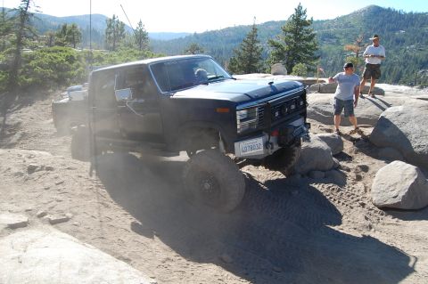 1993 Jeep Wrangler - Modified Ford F-Series pickup truck tackling a challenging off-road course with two people observing.