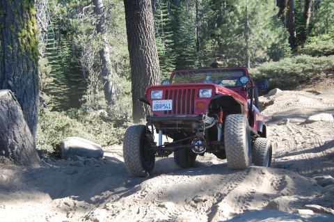 1993 Jeep Wrangler - Red Jeep Wrangler navigates a sandy, wooded trail with a California license plate visible.