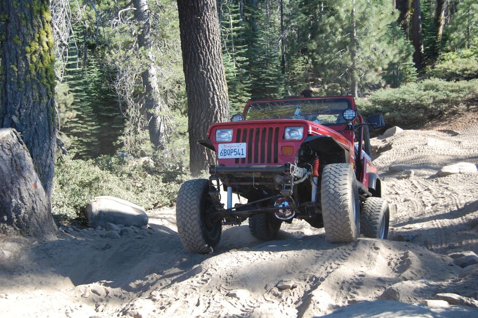 Red Jeep Wrangler on a dirt trail, front view, lifted suspension, large tires, California license plate