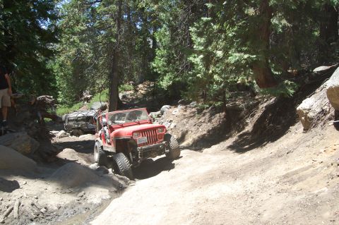 1993 Jeep Wrangler - A red 1993 Jeep Wrangler navigates a challenging off-road trail, with another Jeep following closely behind.