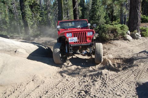 1993 Jeep Wrangler - Red 1993 Jeep Wrangler navigating a dusty, off-road trail through a wooded area.