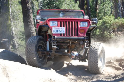 1993 Jeep Wrangler - A red 1993 Jeep Wrangler navigates a dusty, rocky trail through a wooded area.