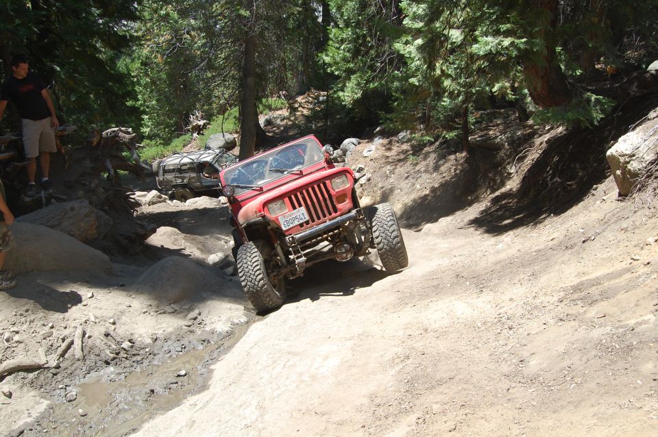 Red Jeep Wrangler on a dirt trail, front grille visible, license plate reads 6BDP643. Another vehicle is behind it