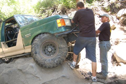 1993 Jeep Wrangler - Modified off-road vehicle navigating a difficult rocky trail with assistance from two people.