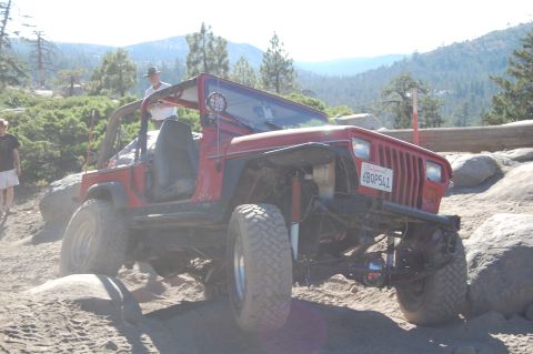 1993 Jeep Wrangler - This red Jeep Wrangler is navigating a challenging off-road course with large rocks and steep inclines.