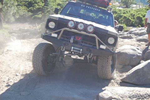 1993 Jeep Wrangler - Off-road vehicle tackling a challenging rocky path with dust clouds forming.