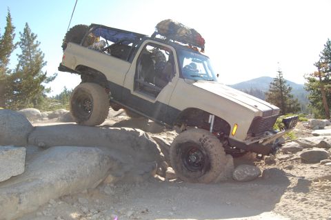 1993 Jeep Wrangler - Modified off-road SUV tackles rocky terrain with its doors removed and a spare tire mounted on the rear.
