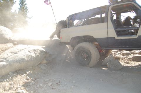 1993 Jeep Wrangler - This modified truck is tackling a rocky trail, with dust and debris flying.