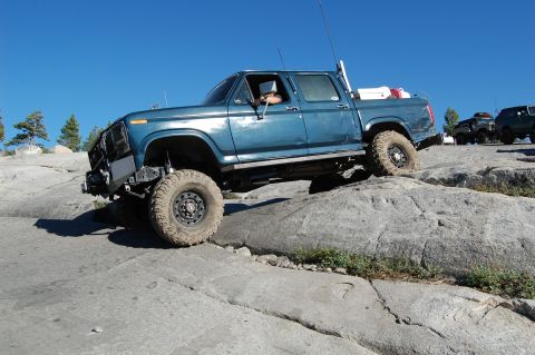 1993 Jeep Wrangler - A blue pickup truck navigates a rocky terrain under a clear blue sky.