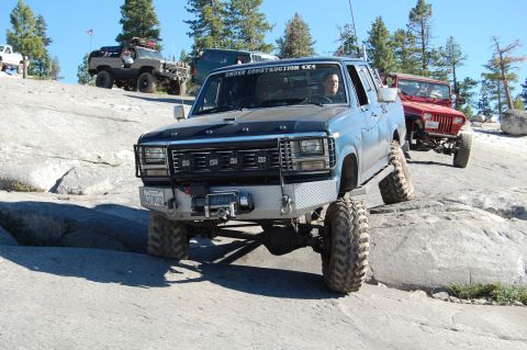 1993 Jeep Wrangler - This modified blue pickup truck navigates a rocky terrain, with another off-road vehicle visible in the background.