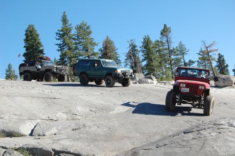 1993 Jeep Wrangler - Three off-road vehicles navigate a rocky trail under a clear blue sky.