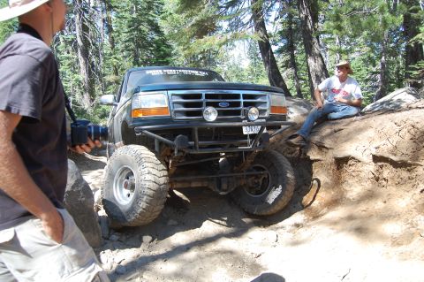 1993 Jeep Wrangler - A modified Ford F-150 navigates an off-road trail with a photographer nearby.