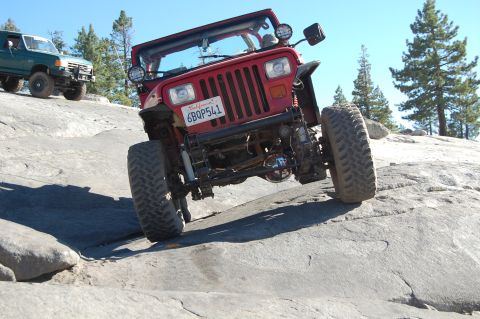 1993 Jeep Wrangler - A red 1993 Jeep Wrangler navigates a rocky trail, its off-road capabilities. Another vehicle is visible in the background.