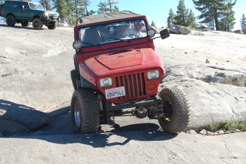 1993 Jeep Wrangler - A red 1993 Jeep Wrangler is shown off-roading on a rocky trail, with another vehicle visible behind it.
