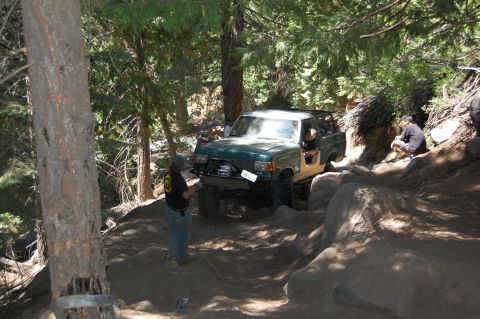 1993 Jeep Wrangler - A green Ford Bronco II navigates a challenging off-road trail surrounded by trees and rocks.