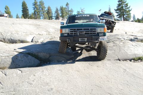 1993 Jeep Wrangler - Two off-road trucks navigate a challenging rocky trail under a clear blue sky.