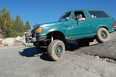 1993 Jeep Wrangler - A green Ford Bronco navigates a challenging rocky terrain under a clear blue sky.