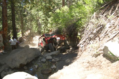 1993 Jeep Wrangler - Two red Jeep Wranglers tackle a challenging rocky trail, kicking up dust as they go.