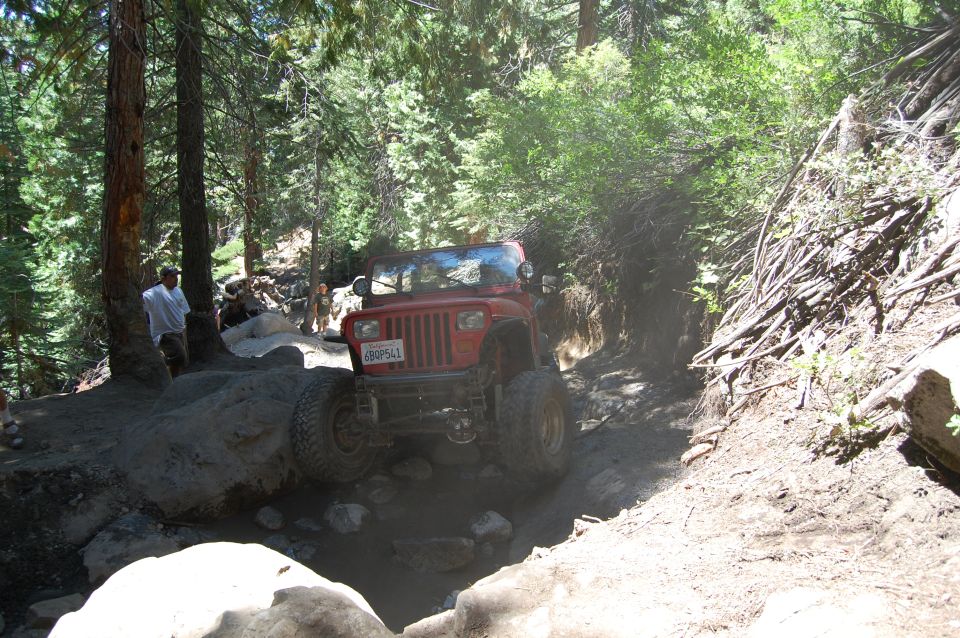Red 1993 Jeep Wrangler navigating a rocky, wooded trail